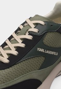 Κοντινό πλάνο στο πράσινο και μαύρο αθλητικό παπούτσι Karl Lagerfeld με μπεζ κορδόνια και λεπτομέρειες από διχτυωτό ύφασμα.