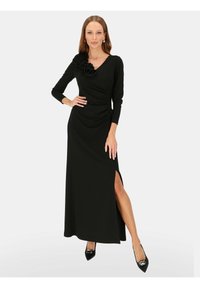 Czarna sukienka z długim rękawem o drapowanym kroju z kwiatowym akcentem na jednym ramieniu. Posiada boczny rozcięcie i prążkowaną fakturę. Czarne, spiczaste buty.