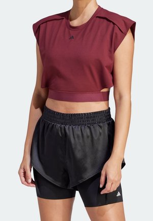 Person wearing a maroon cropped sleeveless top and black layered athletic shorts with fitted black bike shorts underneath.