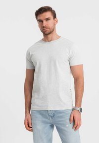 Camiseta gris claro con un sutil patrón de hojas, escote redondo, mangas cortas y un corte relajado. Combinada con jeans de color azul claro.