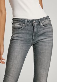 Šedé džíny z denimu s přiléhavým střihem, středně vysokým pasem, pěti kapsami, kovovým knoflíkem a viditelnými švy.
