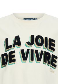 Beige T-Shirt mit kurzen Ärmeln, im Vordergrund mit fettem, mehrfarbigem Glitzertext "LA JOIE DE VIVRE" in schwarzem und türkisfarbenem Akzent.