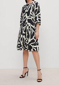 Robe à motif noir et blanc avec une coupe ample, des manches trois-quarts et une taille froncée. Elle est fabriquée dans un tissu lisse et fluide avec une longueur au genou.