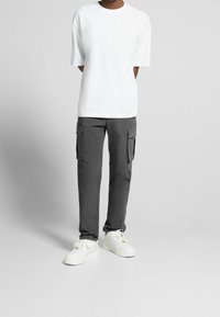 Grå cargobyxor med sidofickor, i kombination med en enkel vit t-shirt och vita sneakers. Enkel design med avslappnad passform och mjukt tyg.