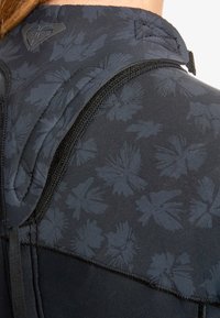 Sort tætsiddende beklædningsgenstand med et blomstermønster i en lidt mørkere nuance, der har synlige syninger og en lynlåsdetalje ved halsen.