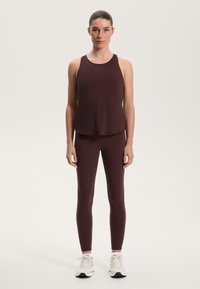 Bordeauxfarbenes Sportoberteil mit rundem Ausschnitt, kombiniert mit passenden Leggings. Der glatte Stoff hat eine leicht elastische Textur. Legere Sneakers runden den Look ab.