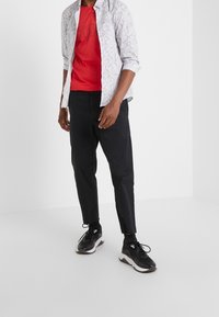 Czerwona koszulka z czarnym logo, biała koszula z wzorem na guziki, czarne zwężane spodnie oraz czarne buty sportowe z białymi akcentami.