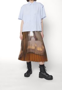 Jasnoniebieska koszula z krótkim rękawem i dwoma przednimi kieszeniami, połączona z plisowaną spódnicą w pikselowym brązowym gradiencie. Uzupełniona czarnymi bootsami wojskowymi.