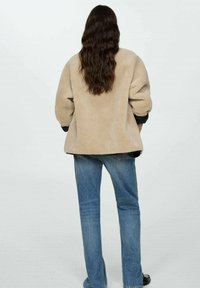 Giacca in pile beige con vestibilità rilassata, spalle cadenti e maniche lunghe. Abbinata a jeans a gamba dritta di colore blu chiaro.