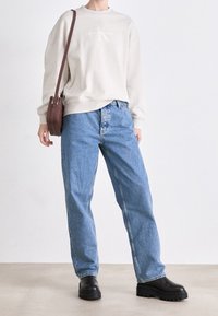 Jasnoszara bluza z logo, jasnoniebieskie luźne dżinsy oraz czarne botki na platformie. Dopełnione brązową torebką na ramię.