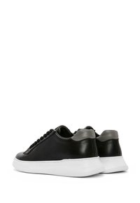 Baskets en cuir noir avec une semelle blanche, présentant un accent de talon gris et un panneau texturé sur les côtés. Design à lacets à l'avant.