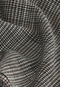 Czarny i biały materiał z teksturowanym wzorem houndstooth, z domieszką jasnoróżowych i szarych włókien, tworzącą subtelny kontrast.