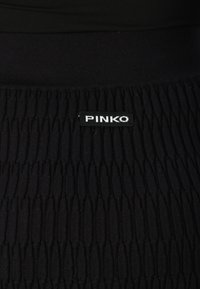 Juodas elastingas sijonas su įbrėžta tekstūra ir vertikaliomis linijomis. Ant juosmens yra prekės ženklo etiketė su baltais užrašais "PINKO".