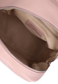 Interno di una borsa a tracolla in pelle rosa con una superficie liscia, fodera beige e chiusura con zip. Etichetta visibile all'interno.
