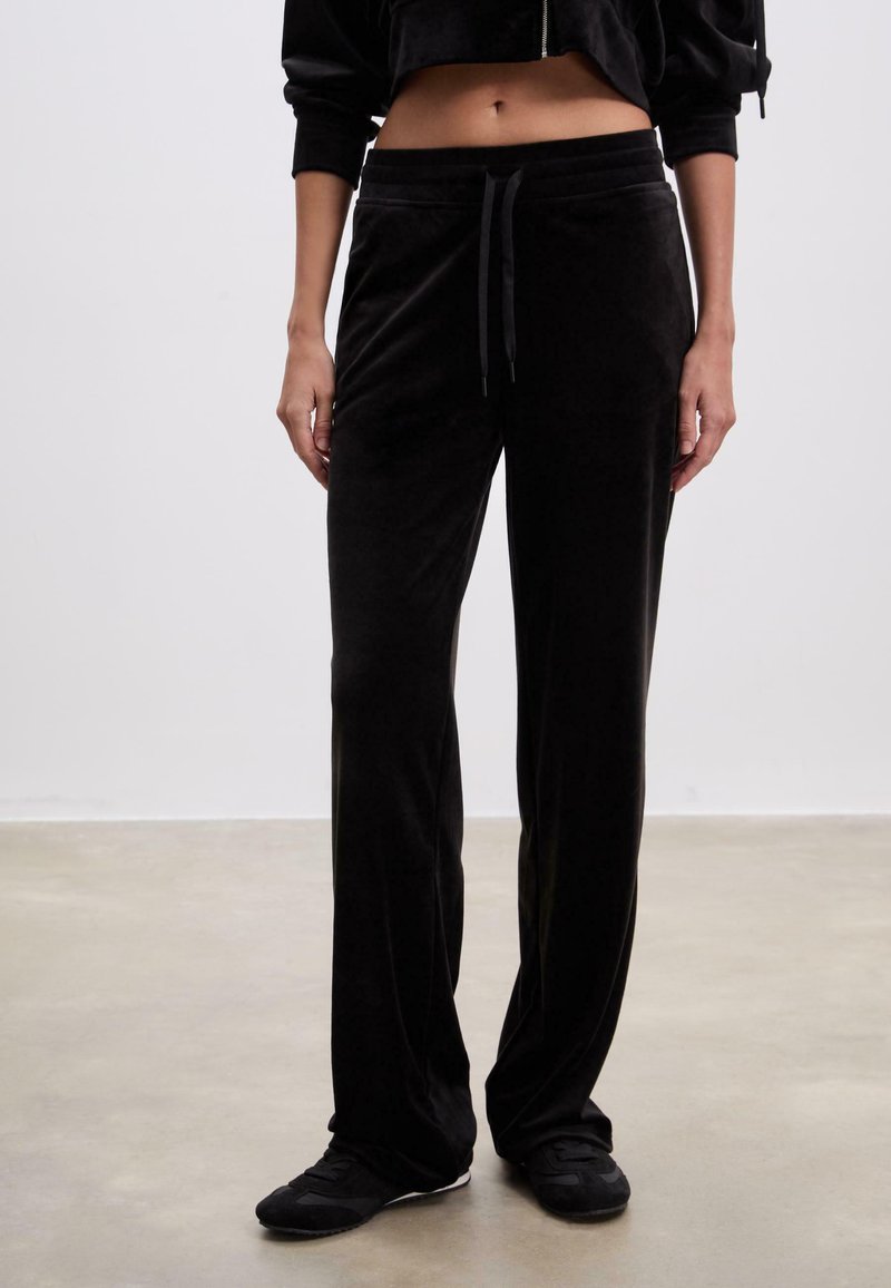 Sorte velour sweatpants med snoretræk i taljen og lige ben, der har en blød tekstur og elastisk talje, parret med sorte sko.