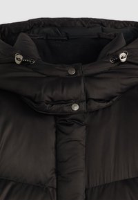 Juoda pūkinė striukė su siuvinėta rašto danga, pamušta vilnoniu, su spaudėmis ir reguliuojama kapišonu su raišteliais.