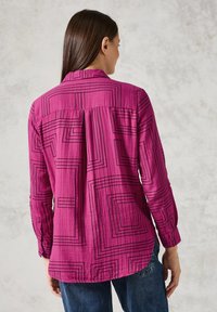 Camicia fucsia a maniche lunghe con motivi geometrici neri, design con colletto e polsini abbottonati, caratterizzata da un dettaglio plissettato sul retro.