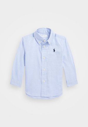 Jasnoniebieska koszula na długi rękaw z guzikami, wykonana z tkaniny bawełnianej. Posiada kołnierzyk, guziki z przodu oraz małe, ciemne logo na lewej piersi.