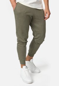 Olijfgroene joggingbroek met een taps toelopend ontwerp, rekbare boorden en zijzakken, gecombineerd met witte sneakers.
