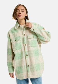 Oversized button-up shirt in roomkleur en mintgroen ruitpatroon. Gemaakt van textuur, donzige stof, met twee borstaspecten en een kraag.