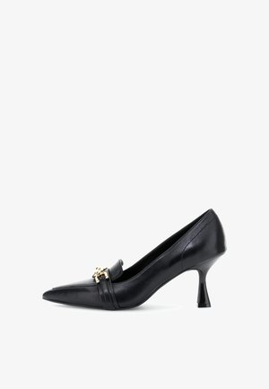 Zapato de tacón alto de cuero negro con punta afilada, que presenta una correa decorativa y herrajes en dorado. El tacón tiene una forma única.