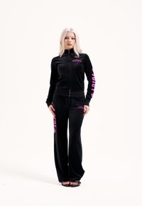 Fekete bársony tréningruha cipzáros dzsekivel és bő szabású nadrággal. Rózsaszín "Juicy" és "Angel" logók díszítik az ujjakat és a lábszárakat.