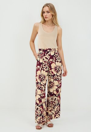Pantaloni larghi floreali in un profondo bordeaux con grandi fiori color crema e beige. Presentano una vita alta e tasche laterali. Abbinati a una canotta beige.