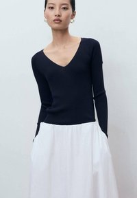 Marinblå ribbad långärmad topp med V-ringning, i kombination med en vit flytande kjol. Outfiten har en minimalistisk design och mjuka texturer.