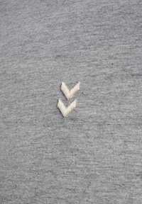 Twee kleine witte chevron-vormige borduurdetails op een achtergrond van gemêleerde grijze stof.