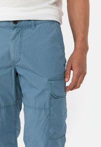 Light blue cargo pants made from lightweight fabric, featuring a side pocket, belt loops, and a button closure. Wrinkled texture visible.