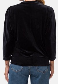 Zwarte fluwelen top met driekwart mouwen, een eenvoudige halslijn en een gladde textuur. Gecombineerd met blauwe spijkerbroek met achterzakken.