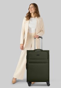 Donkergroene koffer met wielen en een textuurafwerking, een uitschuifbare handgreep en een voorzak met rits, geplaatst op vier wielen voor mobiliteit.