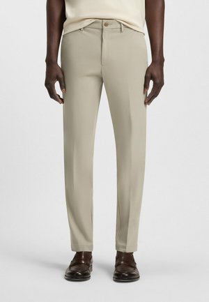 Beige op maat gemaakte broeken met een gladde textuur, rechte pijpen en een knoop tailleband, gecombineerd met donkerbruine loafers.