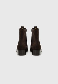 Bottines en daim marron avec un bout arrondi, un talon lisse et des accents en logo doré à l'arrière. Comprend des fermetures éclair sur les côtés pour un enfilage facile.