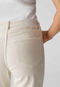 Beige denim jeans met een achterzak, gestikte details en een gladde textuur. De tailleband is licht textured met een label.