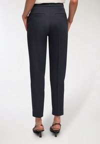 Granatowe spodnie o dopasowanym kroju, z tylnymi kieszeniami i plisą na przodzie. Gładki materiał o eleganckim, nowoczesnym designie.