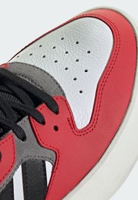 Sneaker in pelle rossa e bianca con dettagli grigi e lacci neri. Presenta dettagli perforati sulla punta e una suola in gomma.