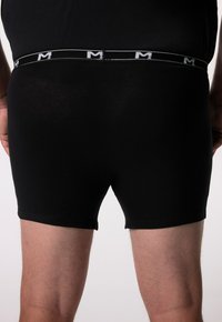 Černé boxerky vyrobené z hladkého materiálu, s kontrastním bílým logem na pásku, těsný střih a zakončené nohavice.