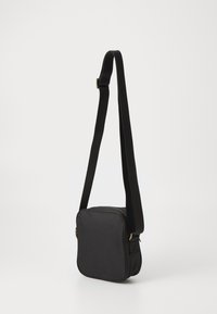 Čierna cez rameno nosená taška z mäkkého textúrovaného materiálu, štvorcového tvaru, so zipsovým uzáverom a nastaviteľným pevným popruhom. Ozdobená zlatými kovovými prvkami.
