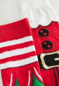 Chaussettes de Noël rouge et blanc avec la ceinture du Père Noël et des accents rayés ; l'une avec un revers en fourrure blanche et l'autre avec un motif festif.