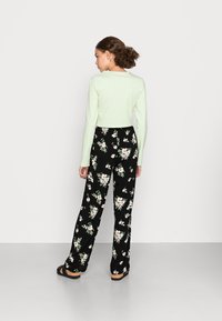 Top cropped de manga longa verde menta combinado com calças largas pretas com padrão floral apresentando uma variedade de flores. Tecidos suaves, ajuste descontraído.