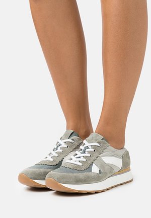 Grå mockasinsneakers med vita detaljer, texturerat tyg och vita snören. Lättvikts gummisula med en ljusbrun yttersula.