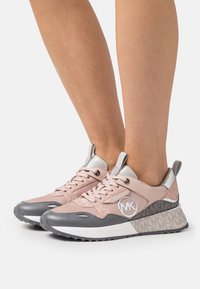 Baskets roses et grises avec une tige texturée, des accents métalliques, un système de laçage et un détail de logo. Présente une semelle intermédiaire à motifs et une semelle en caoutchouc.