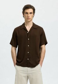 Brun kortärmad skjorta med camp krage, lätt tyg, fem knappar och en avslappnad passform. Randiga byxor kompletterar outfiten.