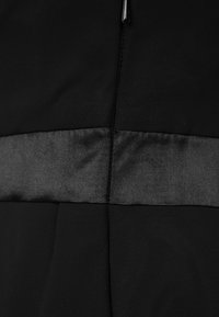 Gros plan sur un tissu noir avec une bande texturée horizontale et une couture verticale qui se croisent au centre.