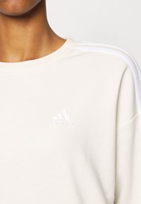 Felpa bianca in cotone con colletto rotondo, texture sottile, tre strisce bianche verticali sulle spalle e logo ricamato sul petto.