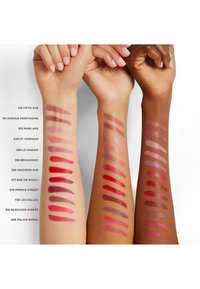 Tre armar som visar 14 läppstiftprover i olika nyanser, från djupa röda till mjuka rosa, på olika hudtoner.