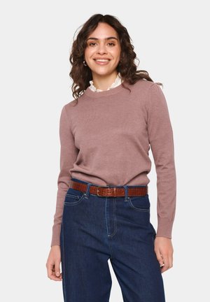 Maglione lavorato a maglia rosa chiaro con scollo a girocollo classico, abbinato a jeans blu scuro e una cintura in pelle marrone con texture. Dettaglio del colletto della camicia arricciato visibile.