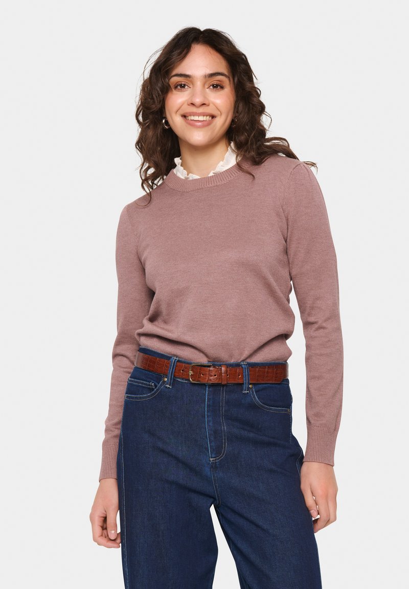Ljust rosa stickad tröja med klassisk rund halsringning, ihopparad med mörkblå jeans och ett brunt texturerat bälte. Detalj med volangkrage synlig.