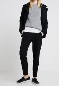 Pull gris côtelé porté sur une chemise blanche, associé à un pantalon noir fuselé et des baskets noires. La veste est sombre et structurée.